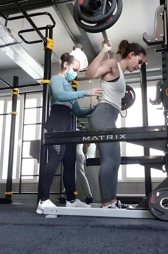 Camille coachant une élève réalisant des squats dans une salle de sport à Lyon
